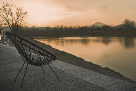 One wicker armchair on the rampart by the river, in the background an early evening landscape with a mountain in the distance.の写真素材