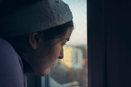 Half profile of a young girl looking at the city through a room window.の写真素材