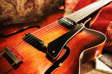 Archtop jazz acoustic guitar on red sofa, vintage look with focus on strings.