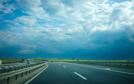 Driving on a highway, a cloudy spring day with sunshine, green fields on the side and new asphalt in...