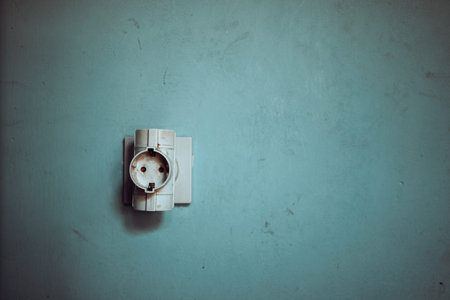 Old plastic power socket plugged in, in the background an old dirty wall.