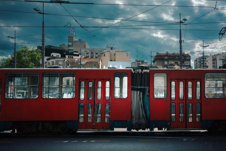 Empty red tram passing by, city surroundings on a cloudy and sunny spring day.の写真素材