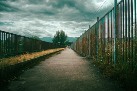 Two little girls on a dramatic sidewalk with a high fence walking to school.の写真素材