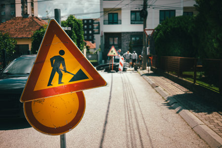 Traffic caution sign, road works, people working on the street can be seen in the background.の写真素材