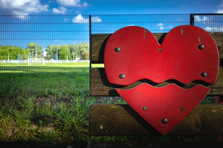 A red wooden heart as a decoration on a bench, a football field in the background.の写真素材