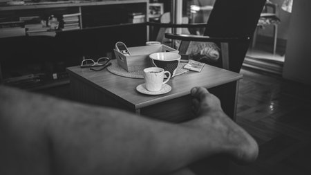 View of an empty coffee cup on the table in the living room, a man is sitting and his bare leg is visible, summer season.の写真素材