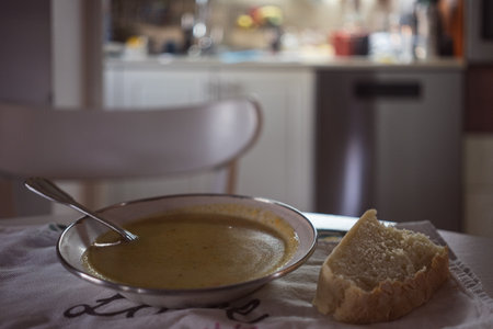 Homemade soup and a piece of homemade bread on the table, kitchen in the background, a scene from ordinary life.の写真素材