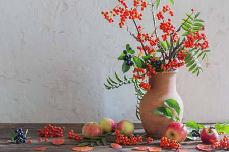 rowan berry and appples in jug on old wooden tableの写真素材