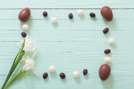 Easter chocolate eggs and flowers on green wooden background