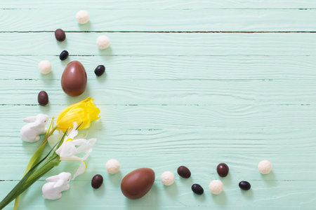 Easter chocolate eggs and flowers on green wooden background