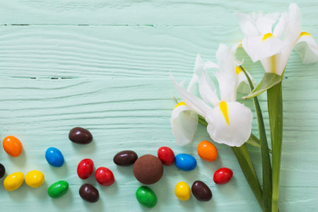 Easter chocolate eggs and flowers on green wooden background
