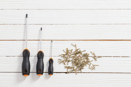 set of screwdrivers and metal screws on white wooden background