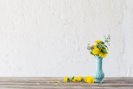 yellow and blue spring flowers s in blue vase on white background