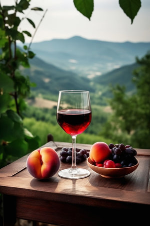 glass of red wine with fruits on wooden table with mountain landscape in backの素材