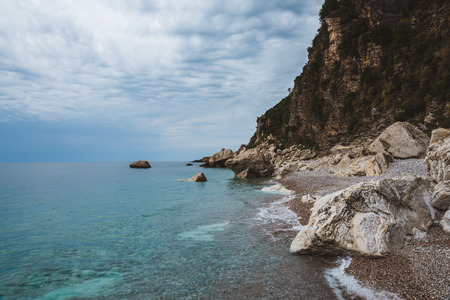Wild scene with sea surf, cloudy sky, stones and rocks. Pebble beach and shoreline in Perazica Do near Rezevichi, Montenegro. Montenegrin coast and Adriatic sea by cloudy day. Montenegro landscape.の写真素材