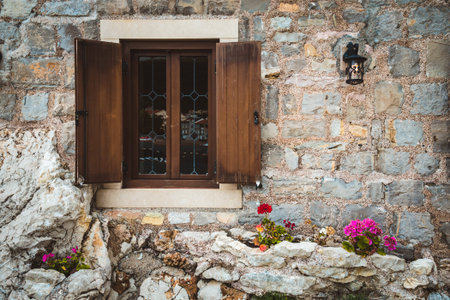 Ancient stone wall, classic old window with wooden shutters, street lantern and flowers on Petrovac,...