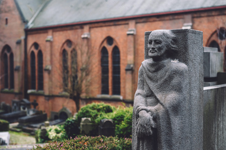 December, 29th, 2016 - Ghent, East Flanders, Belgium. Stone cemetery statue of a man and brick church on Campo Santo historical old graveyard in Sint-amandsberg municipality, Gent.のeditorial素材