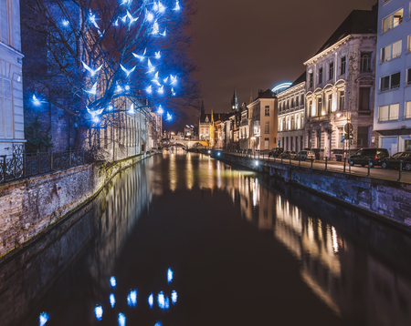 Ghent, Flanders, Belgium - January 3th, 2017. Christmas illuminated birds installation and medieval houses reflected in night canal by evening illumination in historical Gent city center by night.のeditorial素材