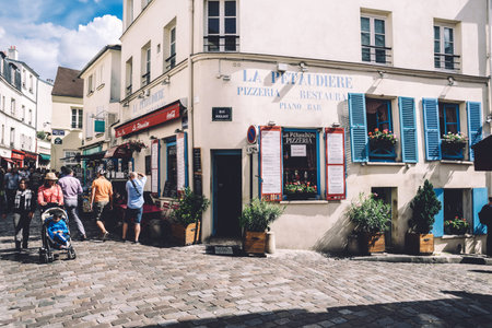 Paris, France - August 10, 2017. Montmartre street and La Petaudiere pizzeria, bar and restaurant, old classical parisian white building facade with blue shutters, greenery in wooden pots and people.のeditorial素材