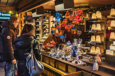 Vienna, Austria - December 24, 2017. Tourists buying souvenirs and gifts at traditional Viennese Christmas market. Illuminated Xmas fair kiosk with candles and colorful glass candle holders at dusk.のeditorial素材