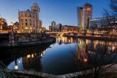 Vienna, Austria - December 29, 2017. Evening view of Wien river with lights and illuminated modern architecture buildings reflected in water. Viennese Danube canal and Urania Observatory at dusk.のeditorial素材