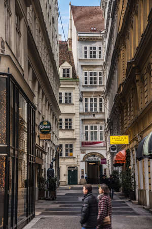Vienna, Austria - December 29, 2017. Central viennese street with walking couple. Old building facades, shops, restaurants, hanging light garlands and seasonal Christmas decoration at sunny day.のeditorial素材
