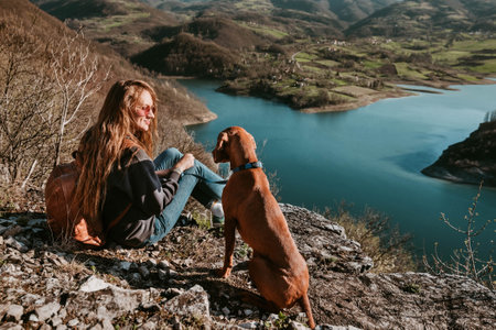 Woman and Vizsla Dog Sitting on Cliff by Riverの写真素材