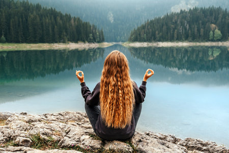 Woman Meditating in Yoga Pose by Mountain Lakeの写真素材