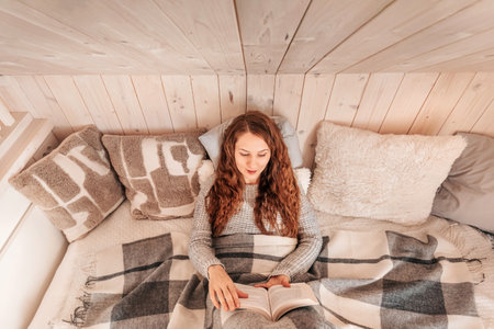 Woman Enjoying Cozy Winter Reading in Bedの写真素材