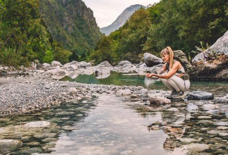 Woman Traveler Washing Hands in Mountain Riverの写真素材