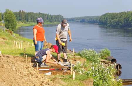 Three archaeologists are looking for small metal objects in the scattered soil with the help of a metal detectorのeditorial素材