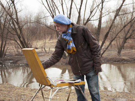 The artist in a beret with an easel paints a landscape in the parkの写真素材