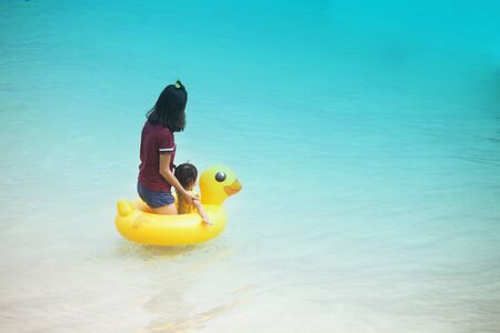 The mother and the girl are in the rubber ring of yellow duck at the beach. In the concept of resting by taking the family to play the beautiful sea. Is another way to cool off in the summer.の写真素材