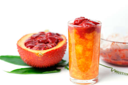 Gac juice in a glass with gac fruit and green leaves on a white background. Tropical fruits that contain antioxidants. Organic food for health.の写真素材