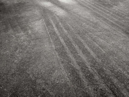 Close up black tire marks on cement floor. Abstract concrete texture in vintage style. Dark background for graphic design or wallpaper. Stains on the road surface caused by the wheels of the car.の写真素材