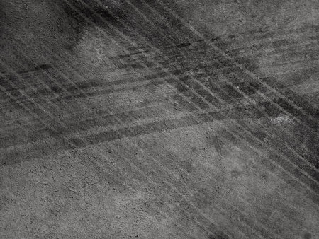 Close up black tire marks on cement floor. Abstract concrete texture in vintage style. Dark background for graphic design or wallpaper. Stains on the road surface caused by the wheels of the car.の写真素材