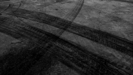 Close up black tire marks on cement floor. Abstract concrete texture in vintage style. Dark background for graphic design or wallpaper. Stains on the road surface caused by the wheels of the car.の写真素材