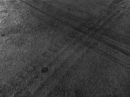 Close up black tire marks on cement floor. Abstract concrete texture in vintage style. Dark background for graphic design or wallpaper. Stains on the road surface caused by the wheels of the car.の写真素材