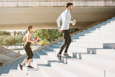 multiethnic couple jogging on stairs in city with water bottleの写真素材