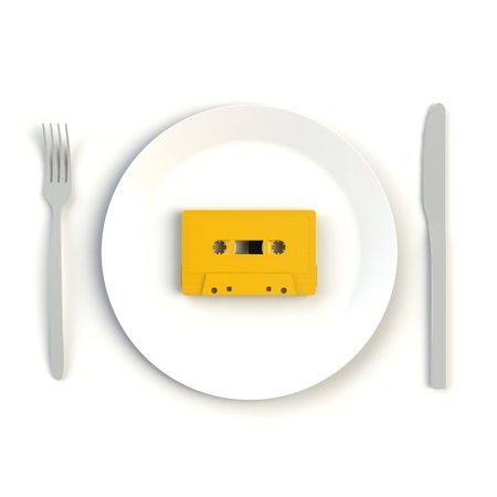 Close up of vintage yellow audio tape cassette on plate, knife and fork on white background, Top view with copy space, 3d renderingの写真素材