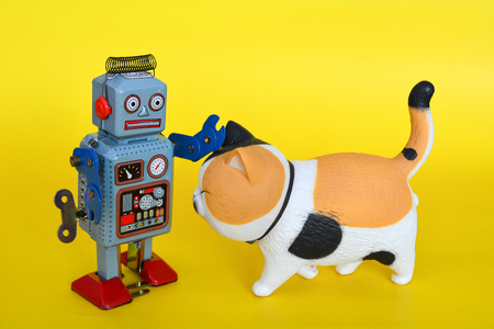 Vintage tin toy robot and a cat isolated on a yellow background.