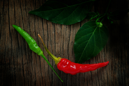 red and green chili pepper with leaves on wooden floorの写真素材