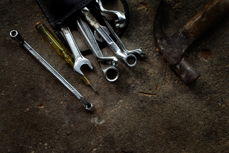 Wrenches in leather bag, screwdriver and hammer put on grunge concrete floor, dark floor background,...