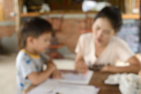 Mother was teaching his son reading a book. Blurred photo background.の写真素材