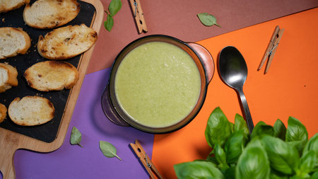 Green fresh broccoli puree soup with garlic croutons on a cutting board and a basil leafの写真素材