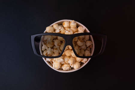 bucket with caramel popcorn and glasses for 3d movies on a black background top view. The concept of...