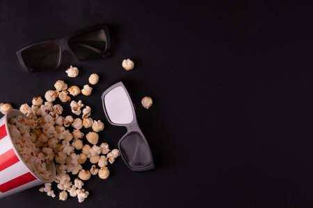 a red and white a scattered bucket of caramel popcorn and glasses for 3d movies on a black background top view. The concept of a banner or advertising for a cinema. Place for textの写真素材
