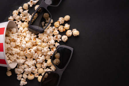 a red and white a scattered bucket of caramel popcorn and glasses for 3d movies on a black background top view. The concept of a banner or advertising for a cinema. Place for textの写真素材