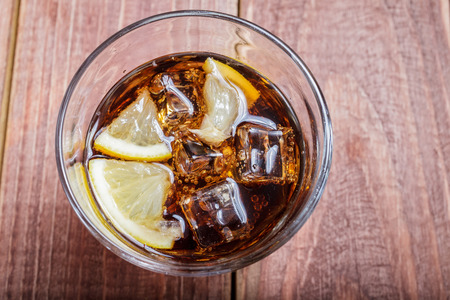 The cooling drink with ice and lemon. Cola in glass on a wooden table. Top viewの写真素材