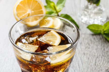 The cooling drink with ice, lemon and mint. Cola in glass on a wooden table.の写真素材